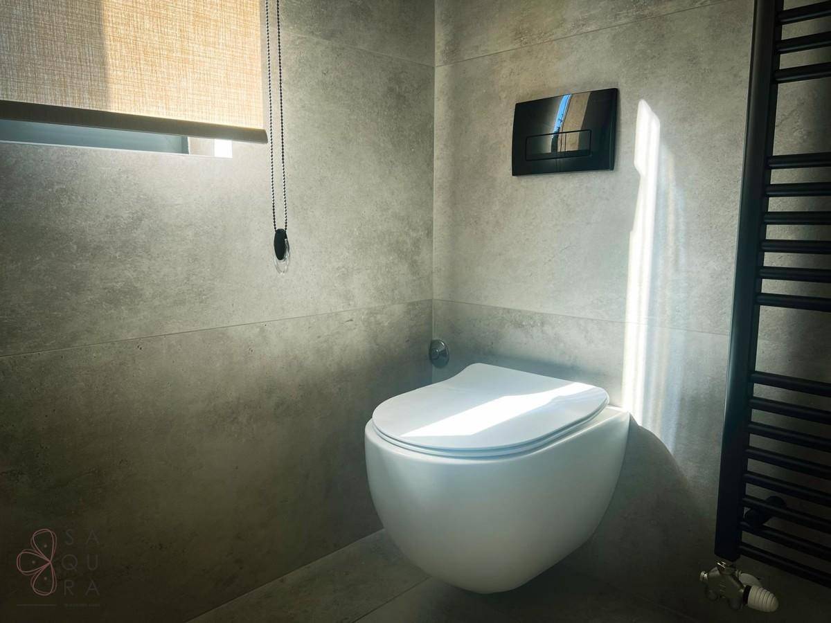 Modernes WC mit wandhängender Toilette, grauen Fliesen und kleinem Fenster.