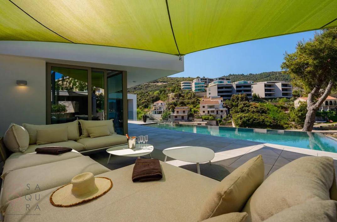 Gemütlicher Außenbereich mit Lounge-Möbeln und Infinity-Pool unter einem grünen Sonnensegel.