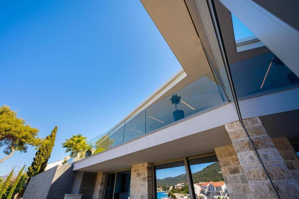 Moderne Architektur der Villa mit Glasgeländern, Steinfassade und weitem Blick auf das Meer.