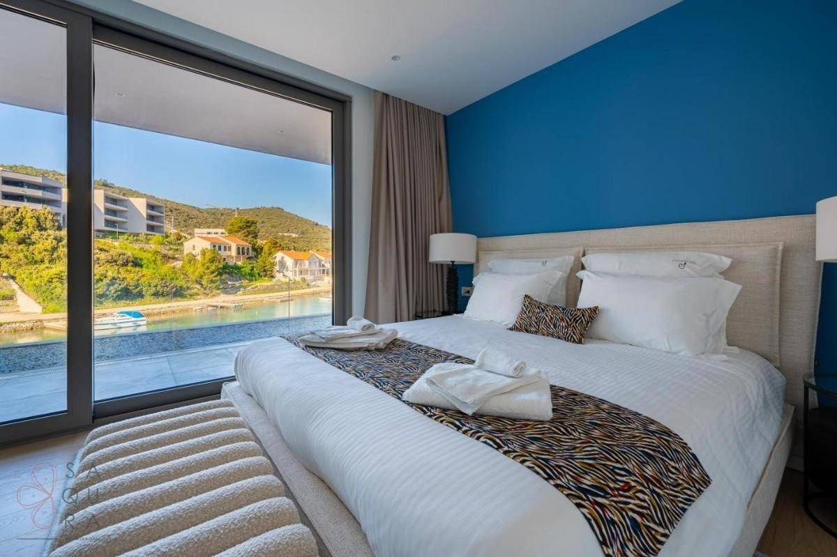 Helles Schlafzimmer mit blauem Akzent und raumhohen Fenstern mit direktem Meerblick.