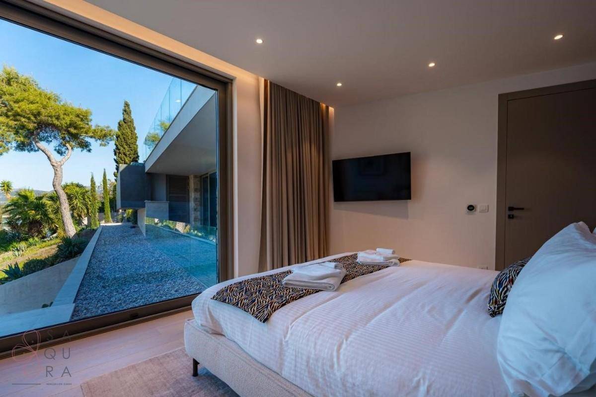 Helles Schlafzimmer mit großem Bett und raumhohen Fenstern mit Blick auf die Außenanlage.