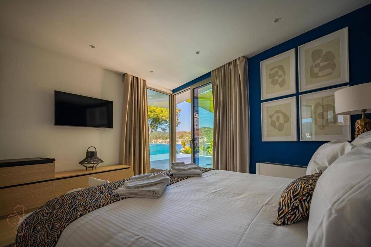 Schlafzimmer mit großem Bett, blauem Akzent und Wandfernseher, mit Zugang zum Außenbereich.
