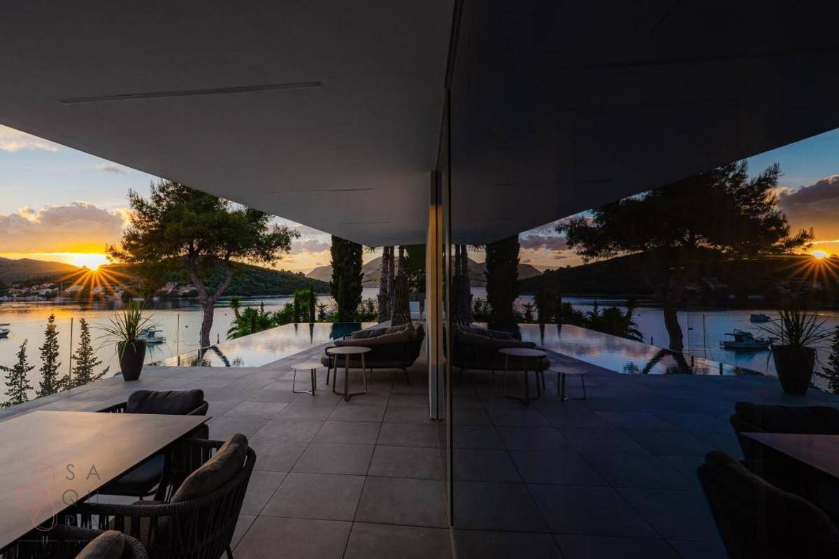 Überdachte Terrasse mit Esstisch und Lounge-Möbeln, ideal für Abendessen mit Meerblick bei Sonnenuntergang.