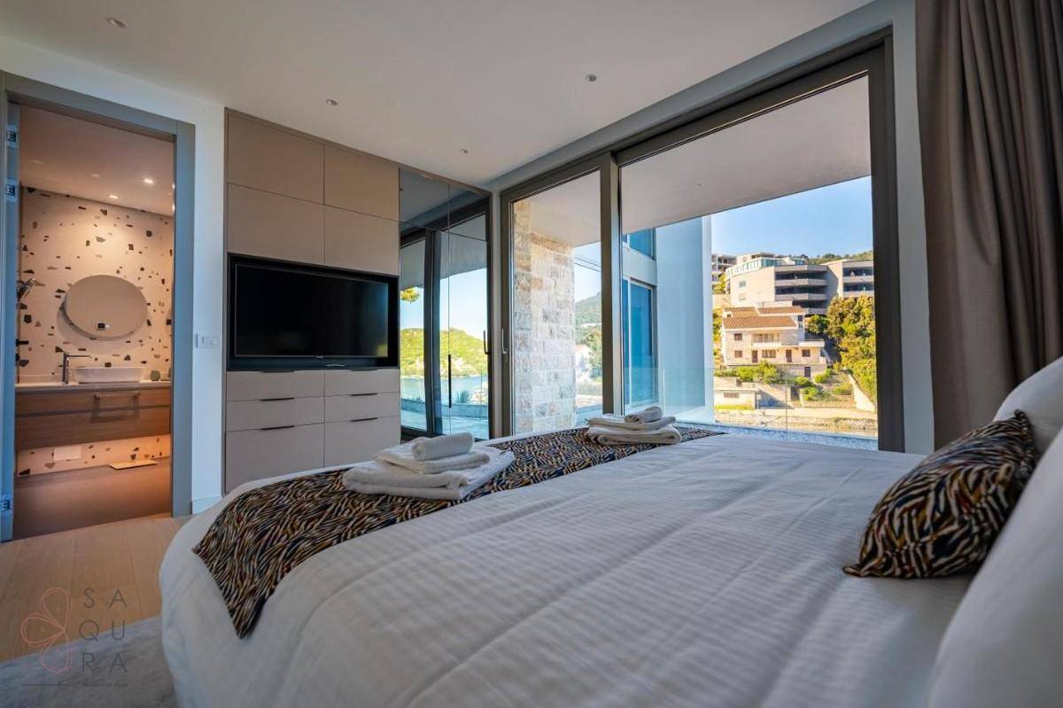 Schlafzimmer mit großem Bett, integriertem TV-Möbel und angrenzendem Badezimmer, mit weitem Ausblick.