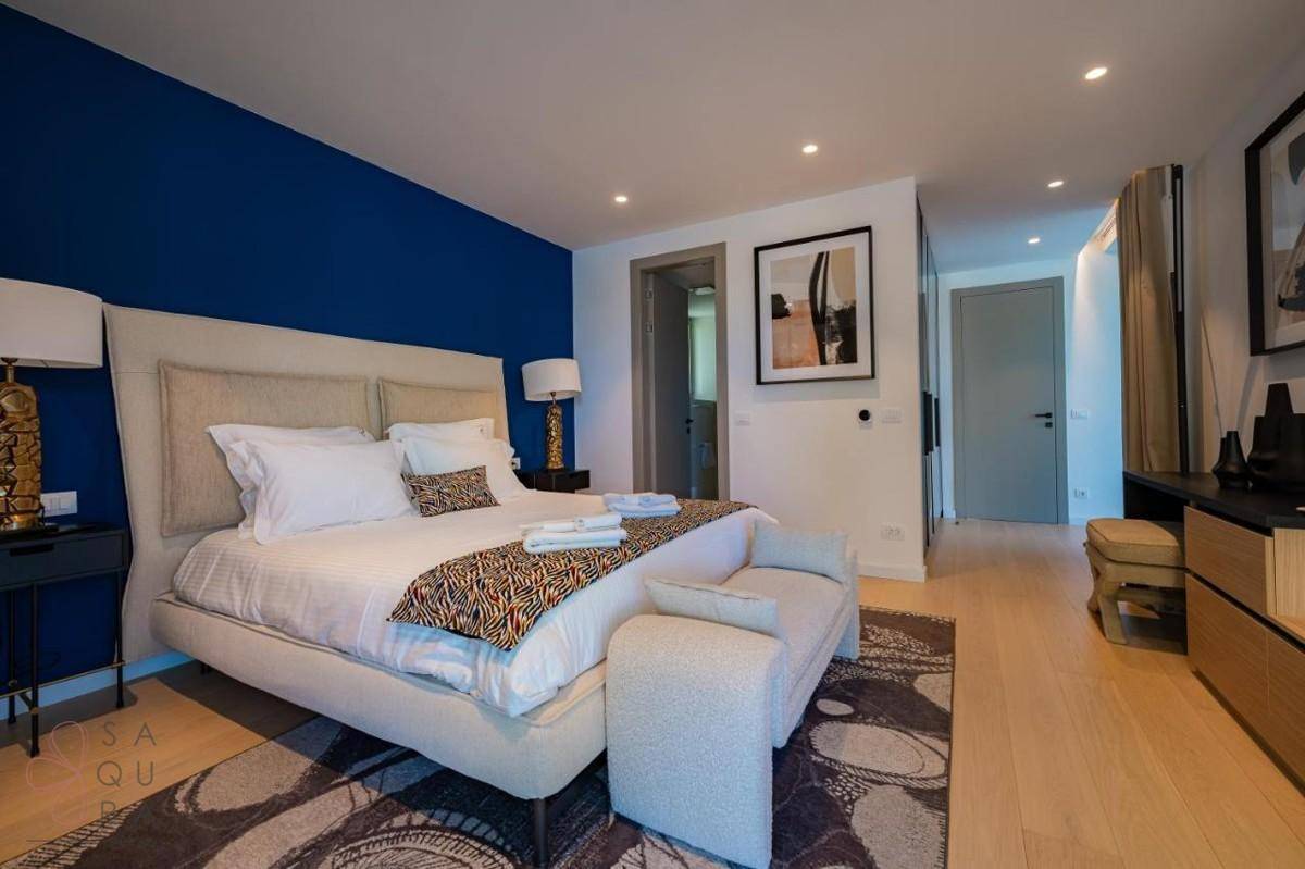 Geräumiges Schlafzimmer mit blauer Wand, beigem Bett und stilvoller Einrichtung, mit Zugang zum Bad.