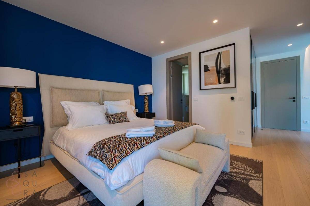 Modernes Schlafzimmer mit blauer Akzentwand, großem Bett und Zugang zu einem Badezimmer.