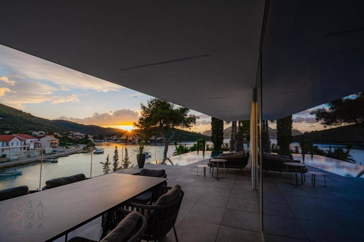Überdachte Terrasse mit Esstisch und Lounge-Möbeln, ideal für Abendessen mit Meerblick bei Sonnenuntergang.