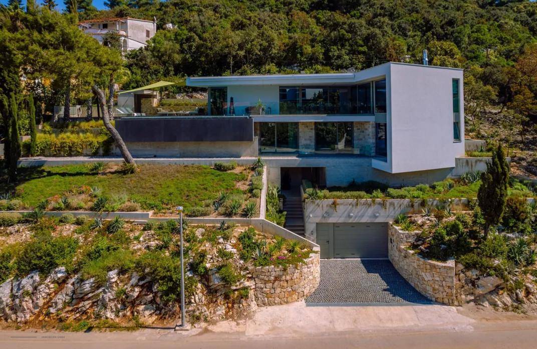 Moderne Villa mit Zufahrt zur Tiefgarage und terrassierter Landschaftsgestaltung am Hang.