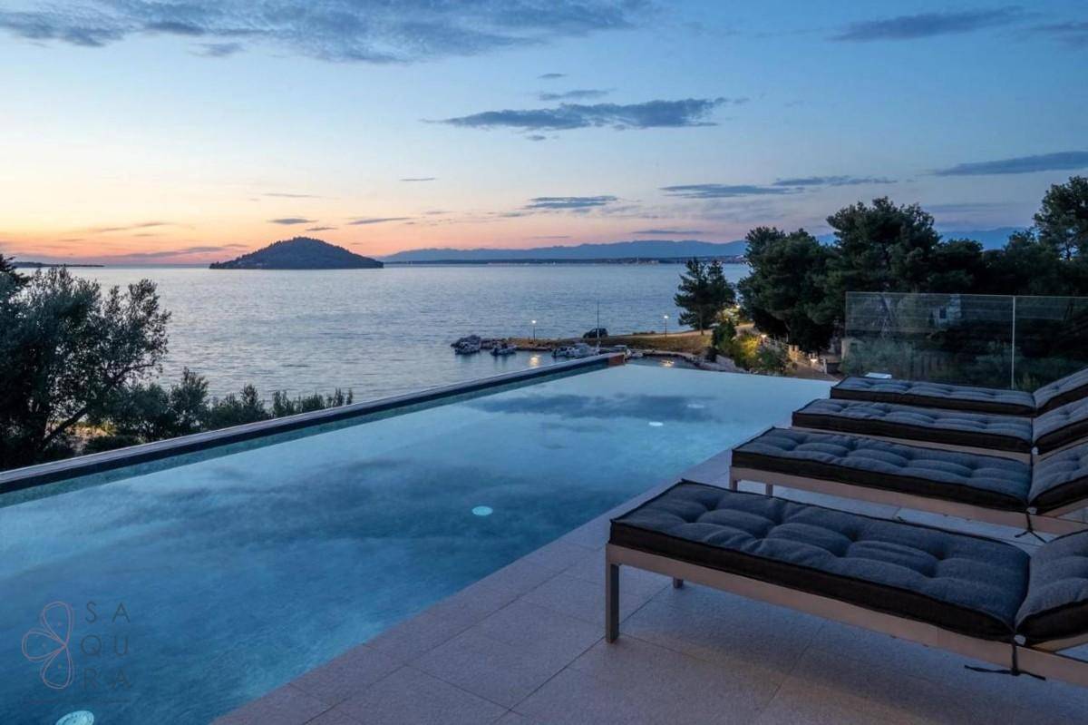 Infinity-Pool mit Liegestühlen bei Sonnenuntergang und malerischem Blick auf das ruhige Meer.