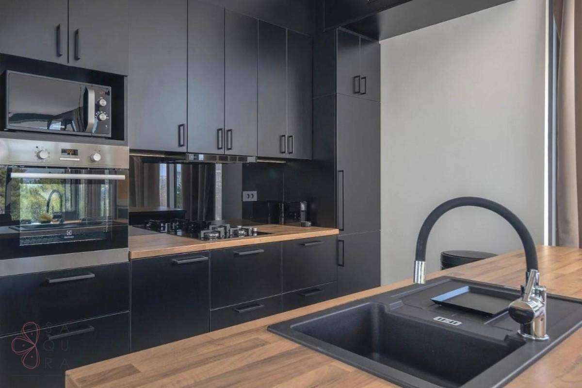 Elegante schwarze Küche mit Holz-Arbeitsplatten, modernen Geräten und integriertem Spülbecken.