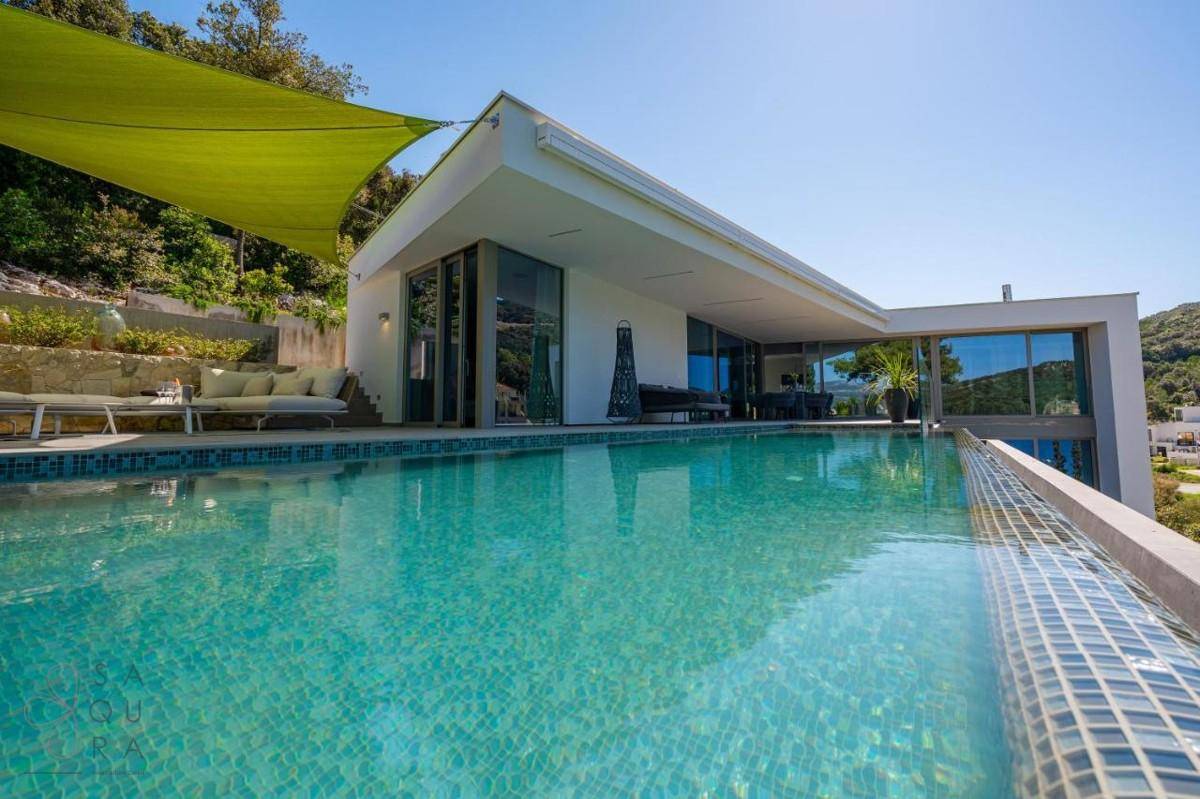 Moderne Villa mit Infinity-Pool und großzügiger Sonnenterrasse in grüner Umgebung.