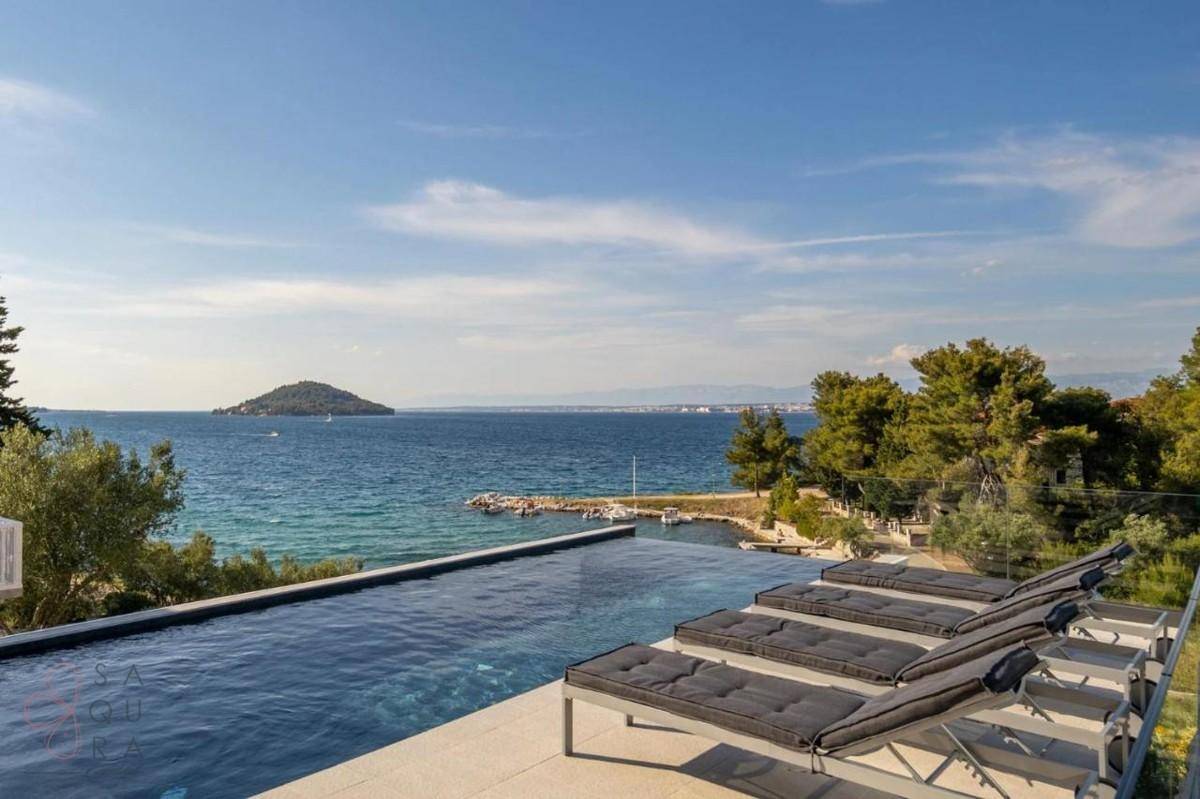 Geräumiger Infinity-Poolbereich mit Liegen und weitem Blick auf das Meer und eine Insel.