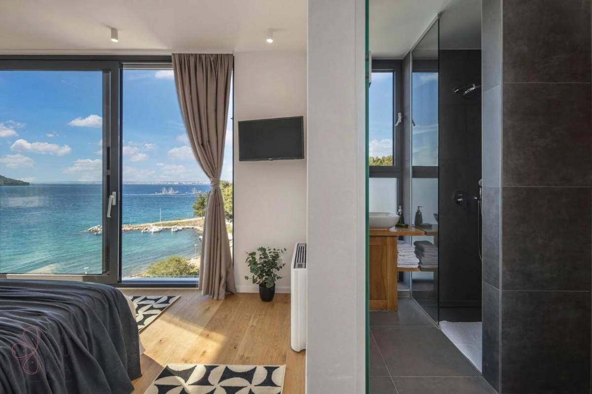 Helles Schlafzimmer mit Meerblick, Holzboden und angrenzendem Badezimmer mit Dusche.