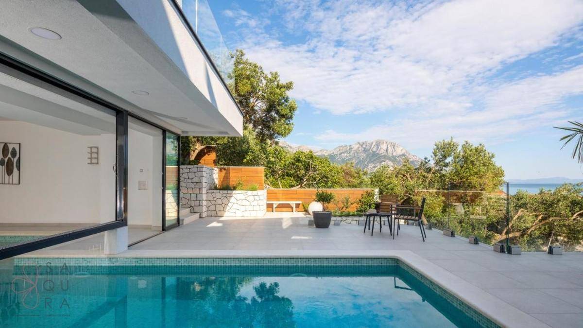 Entspannender Poolbereich mit Terrasse, Sitzgelegenheiten und weitem Blick auf das glitzernde Meer und die Berge.