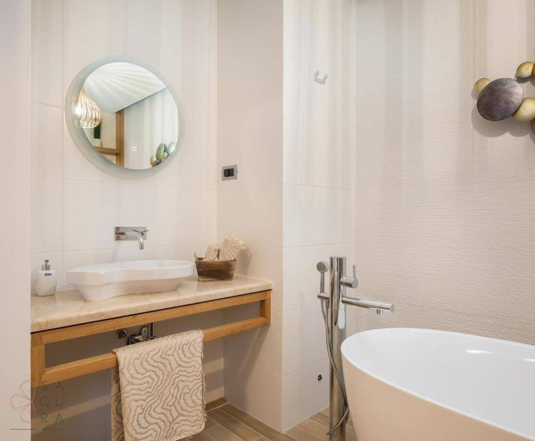 Helles Badezimmer mit freistehender Badewanne, modernem Waschbecken auf Holzunterschrank und rundem Spiegel.