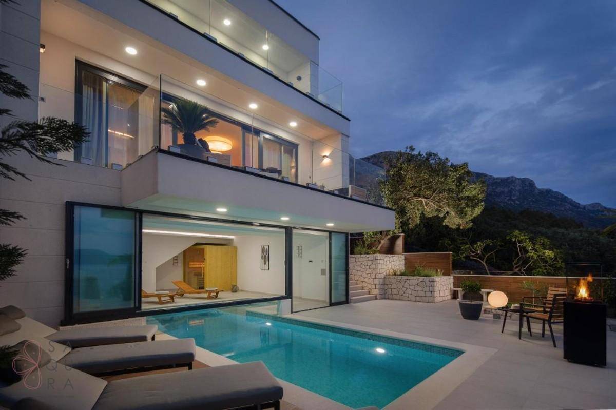 Abendansicht der modernen Villa mit beleuchtetem Pool, gemütlichen Sitzbereichen und stimmungsvoller Beleuchtung.