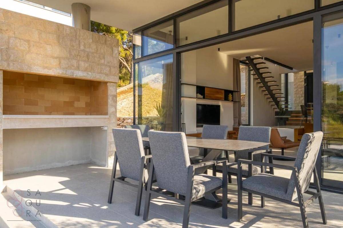 Sonniger Außenbereich mit Esstisch, Stühlen und integriertem Grill, ideal für Mahlzeiten im Freien.