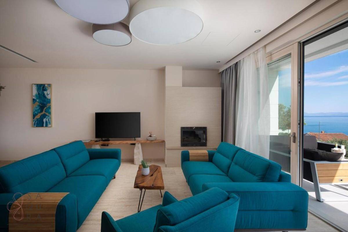 Helles Wohnzimmer mit modernen türkisfarbenen Sofas, Kamin und direktem Zugang zu einem Balkon mit Meerblick.