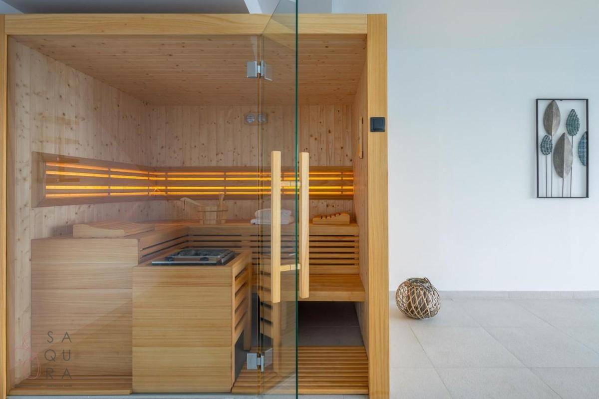 Moderne Sauna mit Glastür, integriert in einen hellen Raum mit Fliesenboden, bereit zur Nutzung.