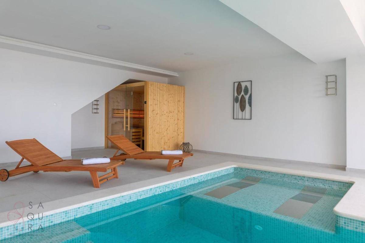 Entspannungsbereich mit Innenpool, bequemen Sonnenliegen und einer sichtbaren Sauna im Hintergrund.
