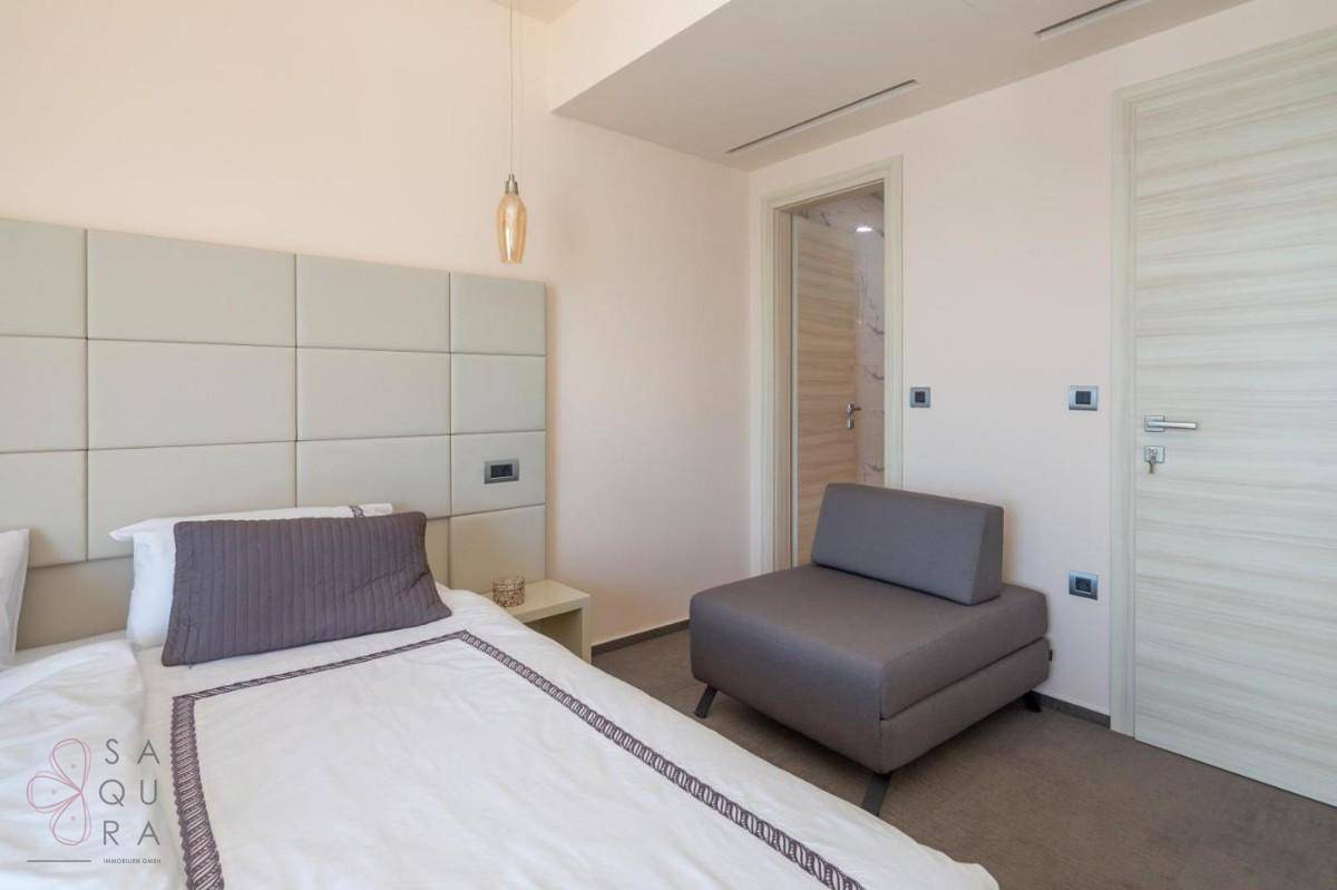 Komfortables Schlafzimmer mit Einzelbett, modernem Sessel und Zugang zu einem angrenzenden Badezimmer.