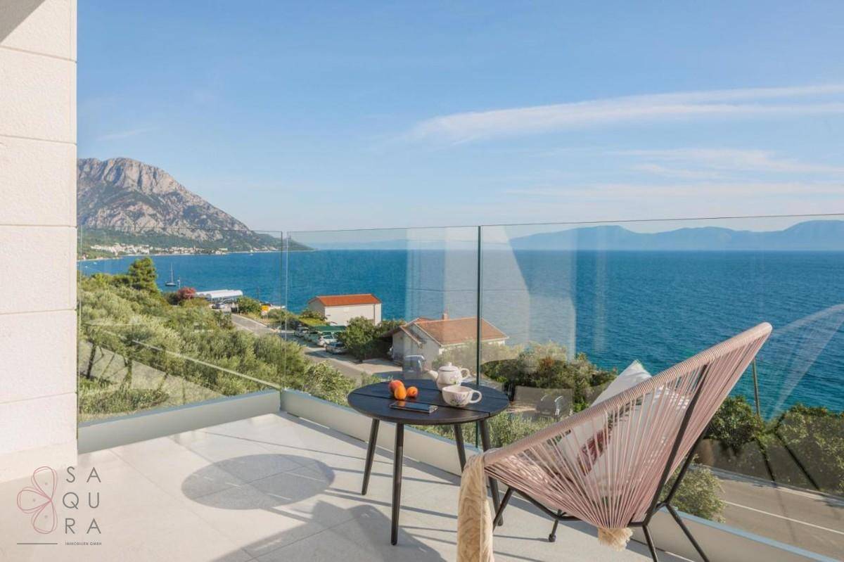 Sonniger Balkon mit Sitzgelegenheit und atemberaubendem Panoramablick auf das Meer und die umliegenden Berge.