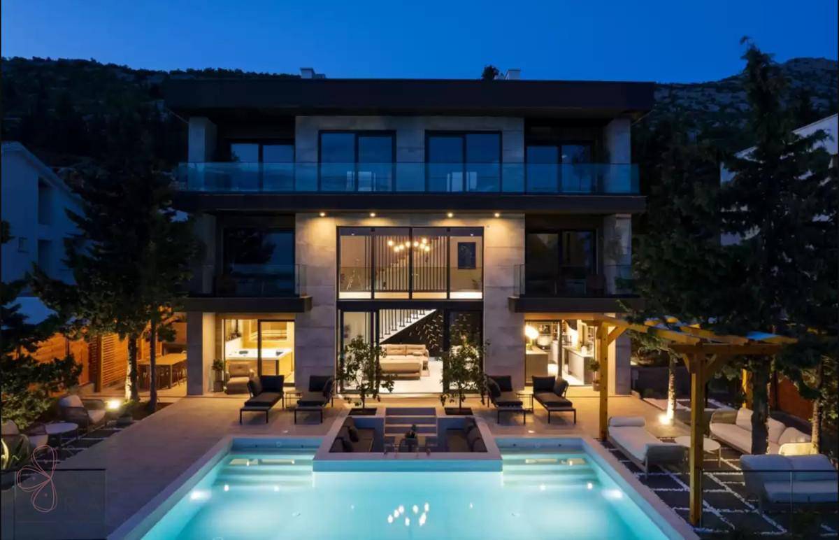 Beleuchtete moderne Villa bei Nacht mit großem Pool und einladenden Außenbereichen.