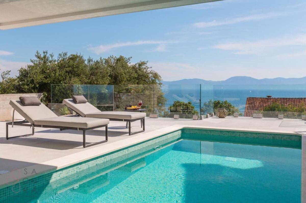 Sonniger Poolbereich mit bequemen Sonnenliegen und weitem, unverbautem Blick auf das blaue Meer.