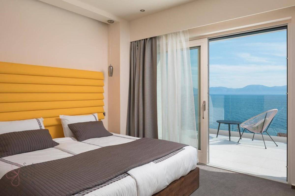 Helles Schlafzimmer mit zwei Einzelbetten, gelbem Kopfteil und Balkonzugang mit weitem Meerblick.
