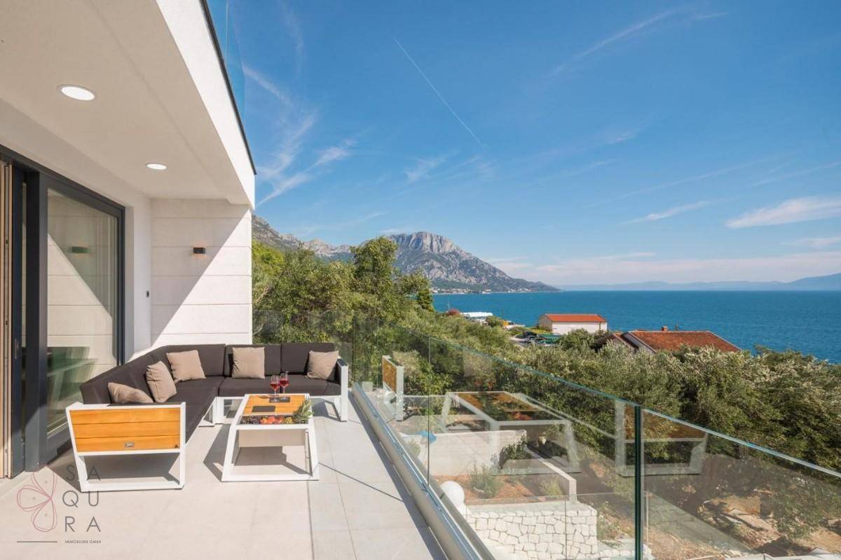 Heller Balkon mit bequemen Lounge-Möbeln und weitem Blick auf das Meer und die umliegenden Berge.