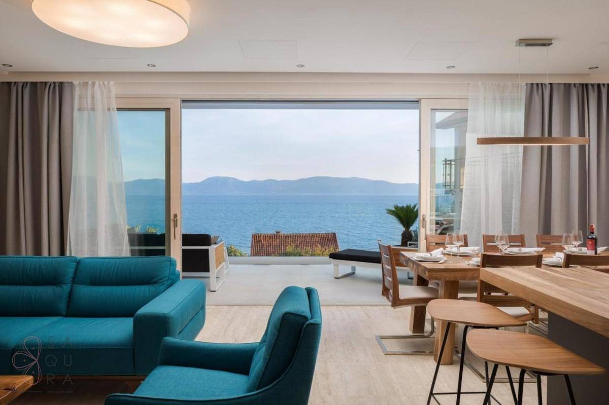 Offener Wohn- und Essbereich mit Meerblick, blauen Sofas und Holztisch.