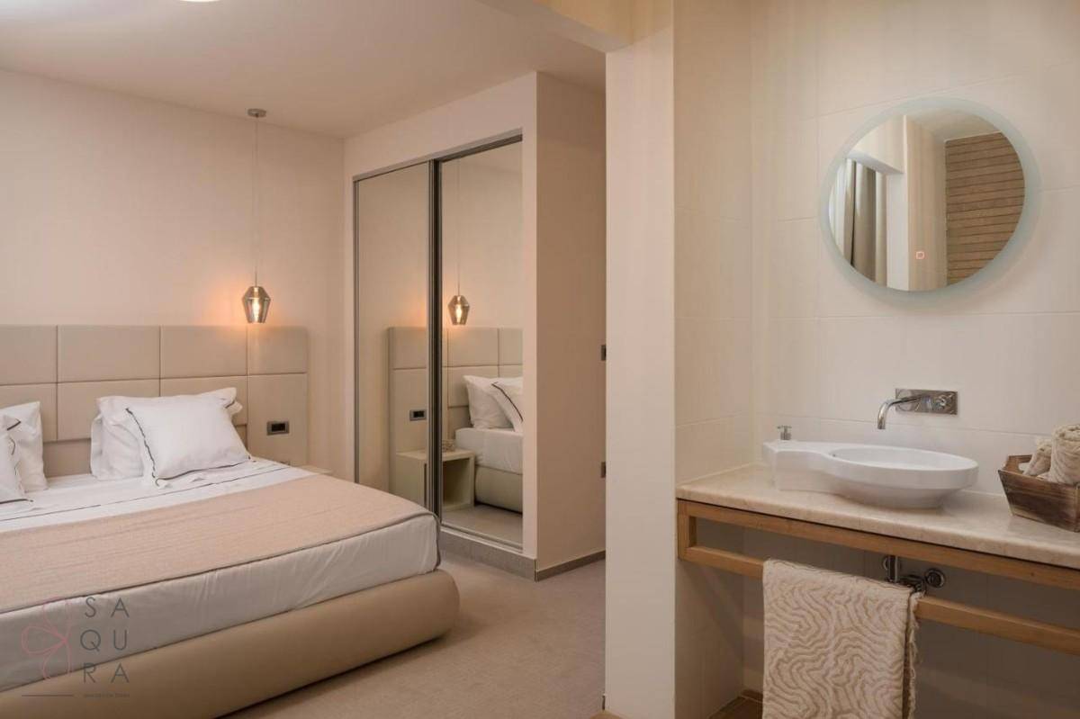 Schlafzimmer mit integriertem Badezimmerbereich, modernem Waschbecken und Spiegelschrank.
