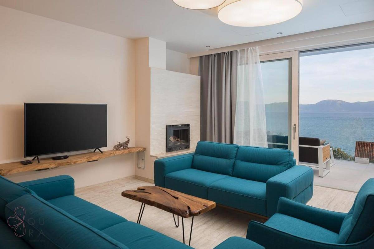 Gemütliches Wohnzimmer mit Kamin, blauen Sofas und Meerblick durch große Fenster.