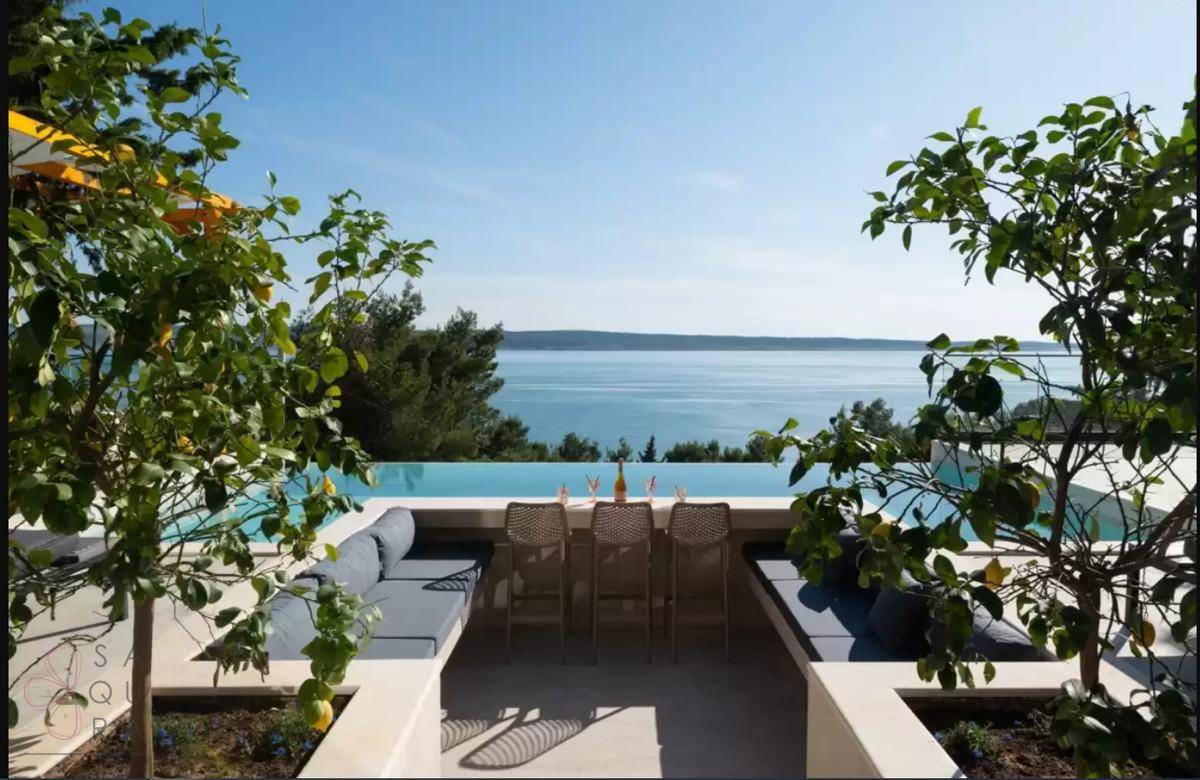 Sonniger Außenbereich mit eingelassener Lounge, Pool und weitem Blick auf das glitzernde Meer.