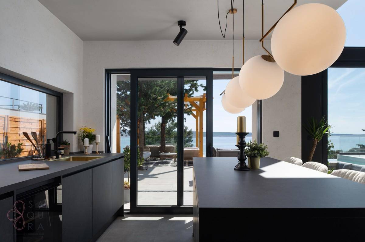 Moderne schwarze Küche mit Kochinsel und direktem Zugang zur Terrasse mit Meerblick.