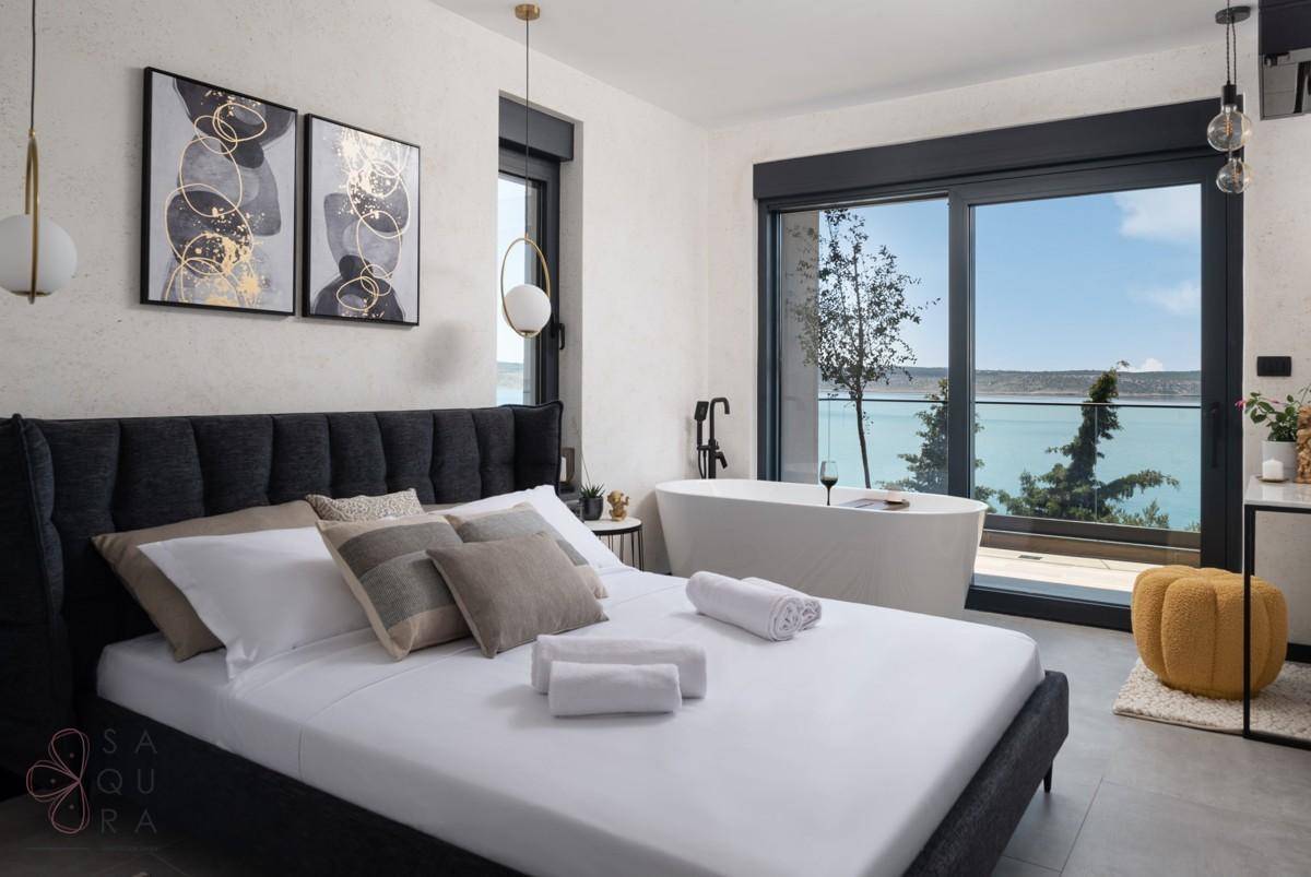 Luxuriöses Schlafzimmer mit freistehender Badewanne und direktem Zugang zu einem Balkon mit Meerblick.
