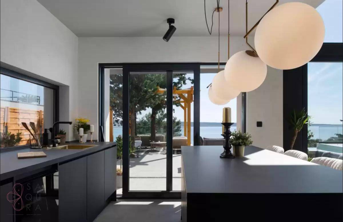 Moderne schwarze Küche mit Kochinsel und direktem Zugang zur Terrasse mit Meerblick.