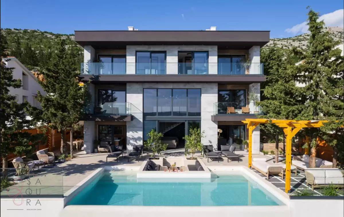 Moderne Villa mit großem Poolbereich, weitläufigen Terrassen und zeitgenössischer Architektur unter blauem Himmel.
