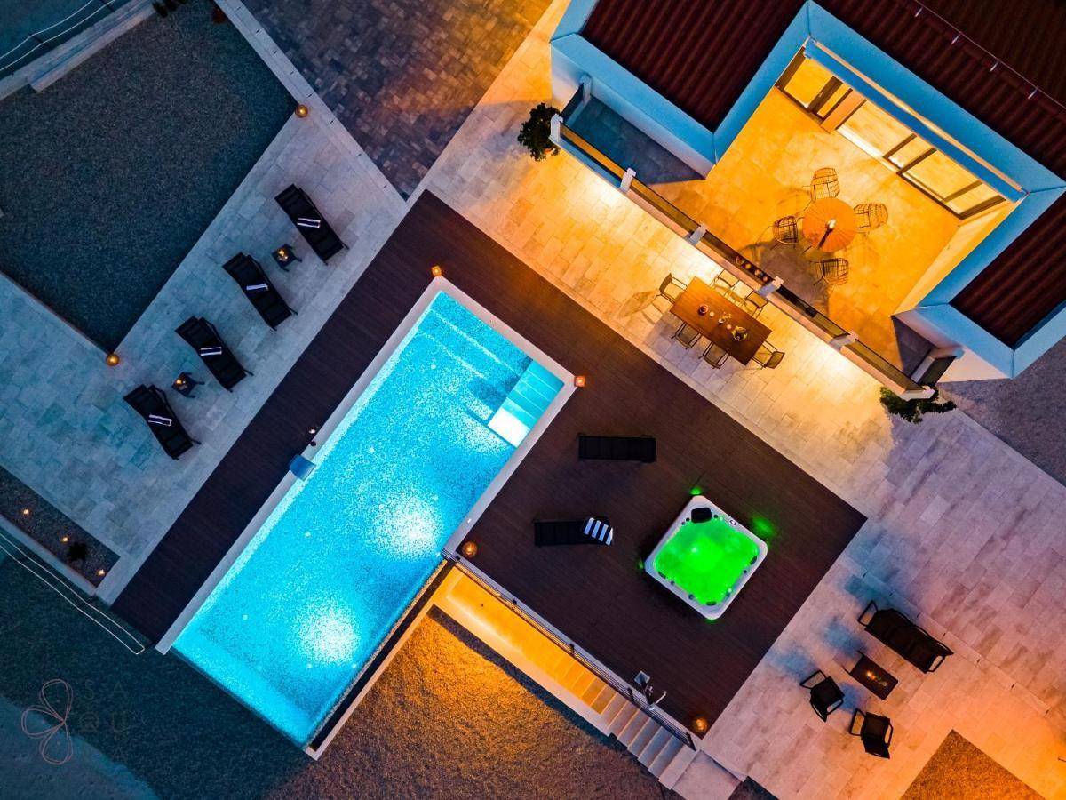 Luftaufnahme der Villa bei Nacht mit beleuchtetem Pool, Whirlpool und verschiedenen Sitzbereichen.