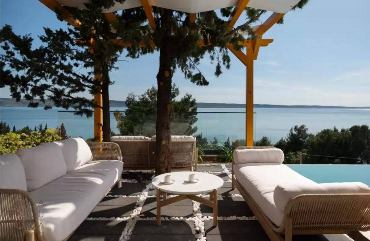 Gemütliche Terrasse mit Lounge-Möbeln unter einer Pergola und weitem Blick auf das Meer.