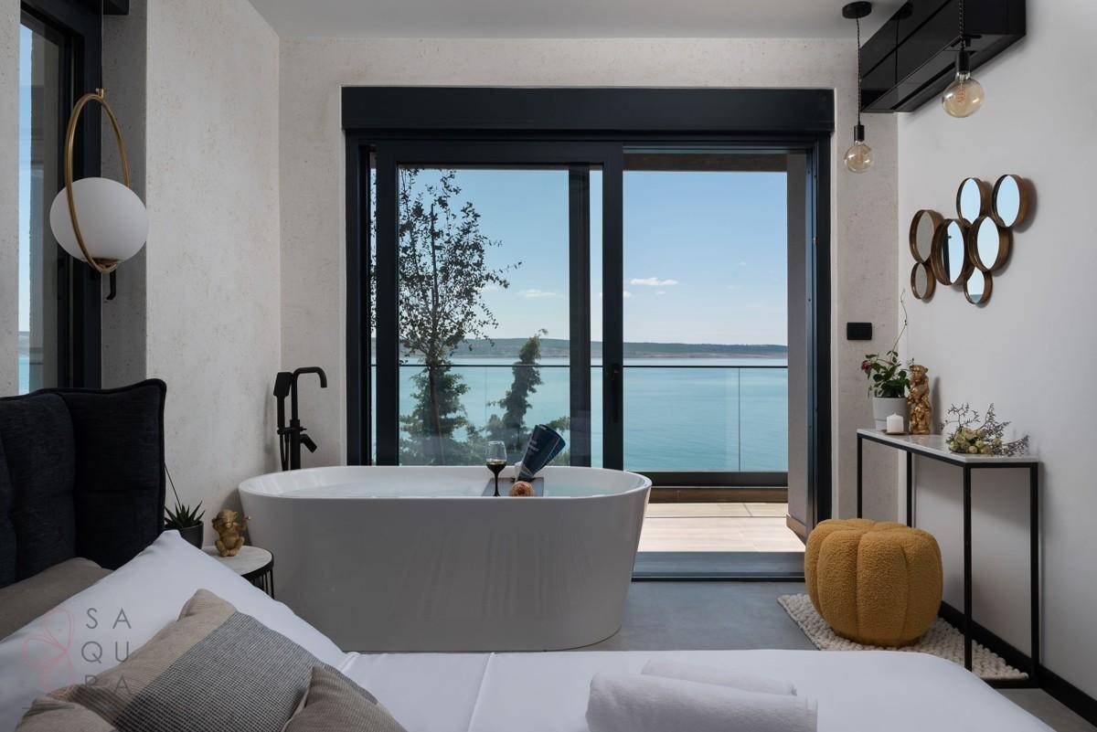 Luxuriöses Schlafzimmer mit freistehender Badewanne und direktem Zugang zu einem Balkon mit Meerblick.