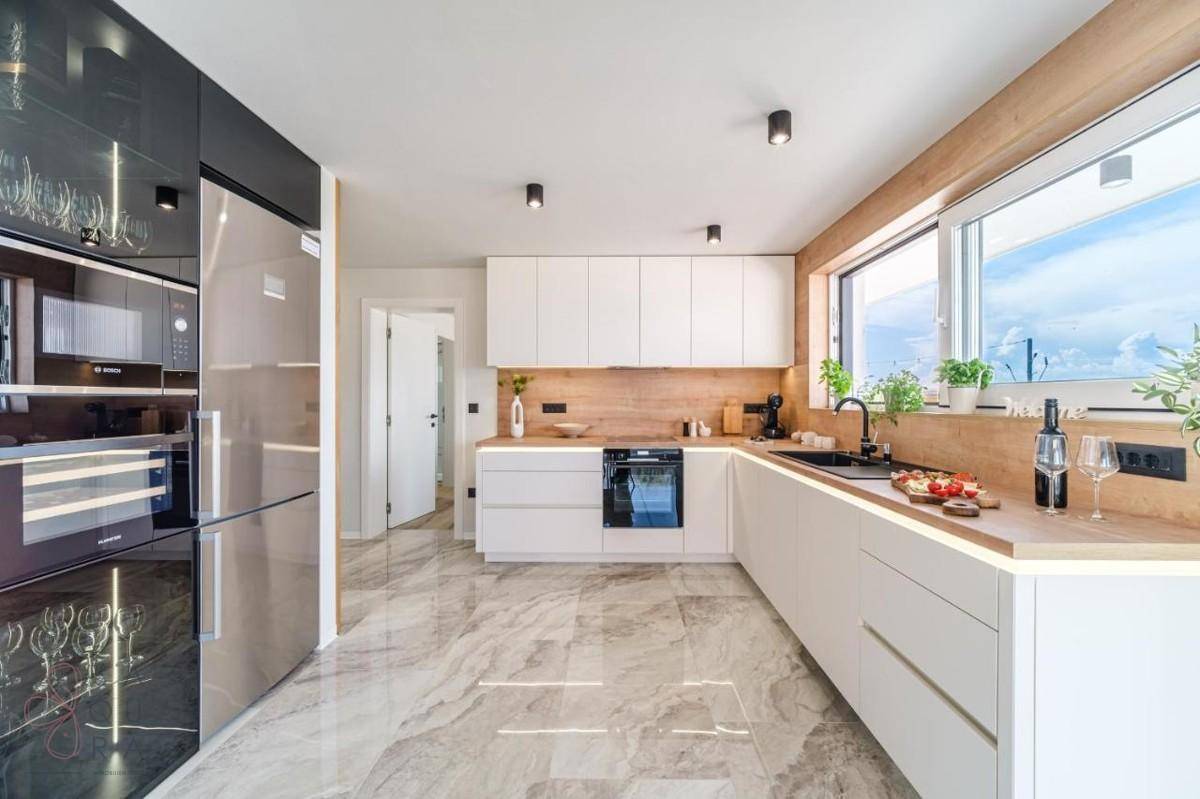 Moderne Einbauküche mit weißen Fronten, Holzdetails und integrierten Geräten.