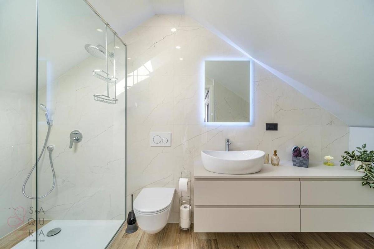 Elegantes Badezimmer mit moderner Ausstattung, begehbarer Dusche und beleuchtetem Spiegel.