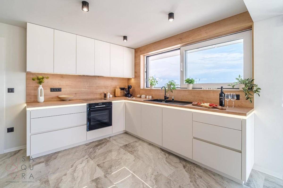Helle, moderne Küche mit weißen Schränken, Holz-Arbeitsplatten und großem Fenster.
