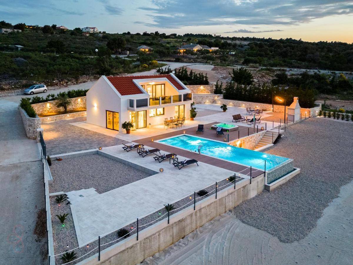 Weitläufige Außenanlage der modernen Villa mit Pool, Whirlpool und Grillplatz bei Dämmerung.