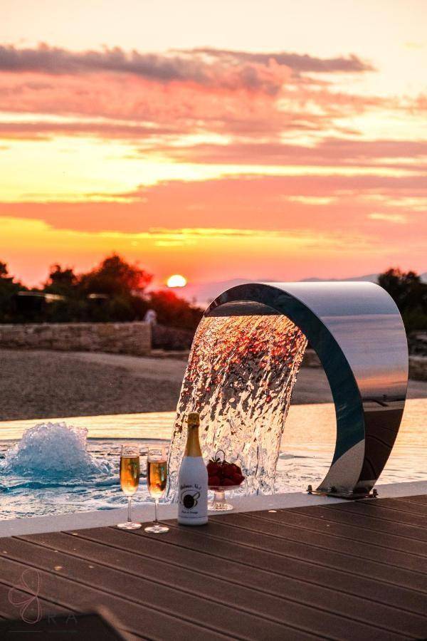 Detailaufnahme eines Wasserfalls am Poolrand mit Champagner und Früchten bei Sonnenuntergang.