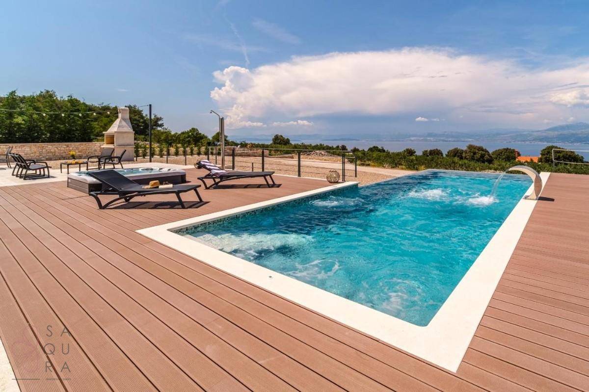 Großer Pool mit Holzdeck, Sonnenliegen und Blick auf das Meer und die Landschaft.