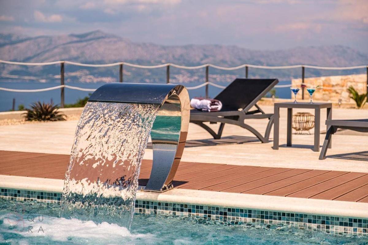 Entspannungsbereich am Pool mit Wasserfall und weitem Blick auf das Meer und die Berge.