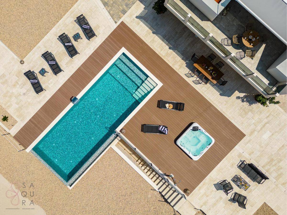 Nahaufnahme der Außenanlage von oben mit Pool, Whirlpool und Holzdeck.