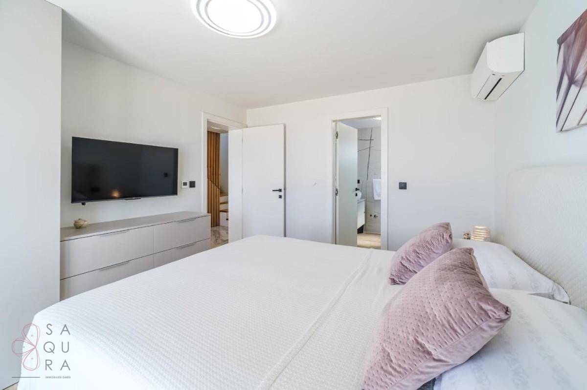 Modernes Schlafzimmer mit Doppelbett, Wandfernseher und Zugang zu einem Badezimmer.